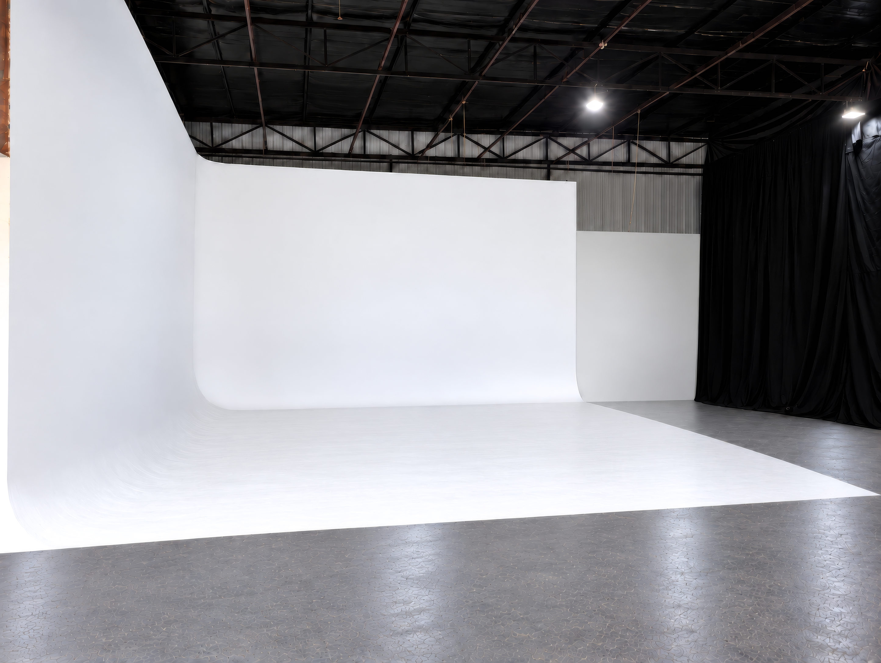 White cyclorama wall beside black drapes under a steel roof